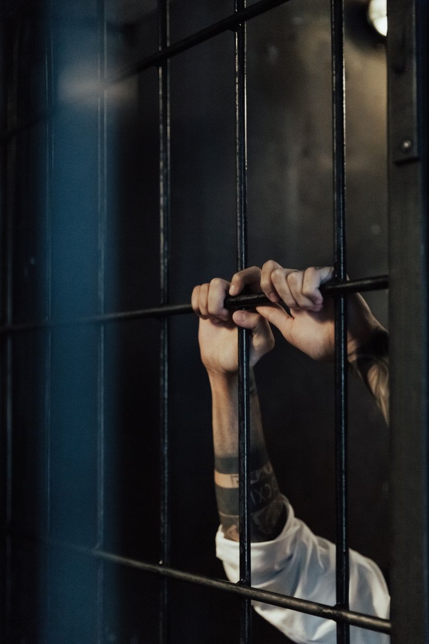 hands of a person holding on metal railings in a jail